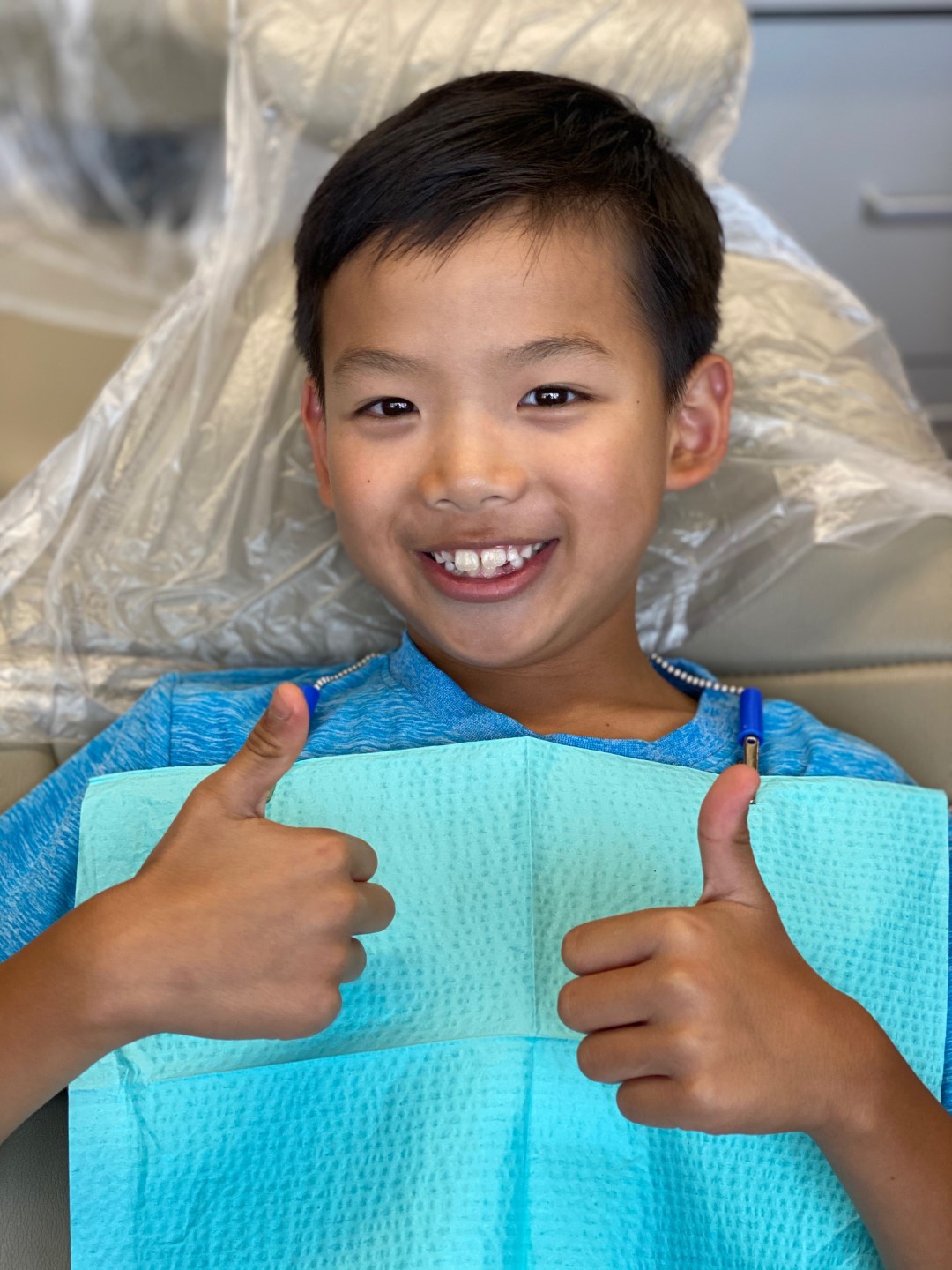 Smiling young boy giving thumbs up while wearing dental bib in dentist chair